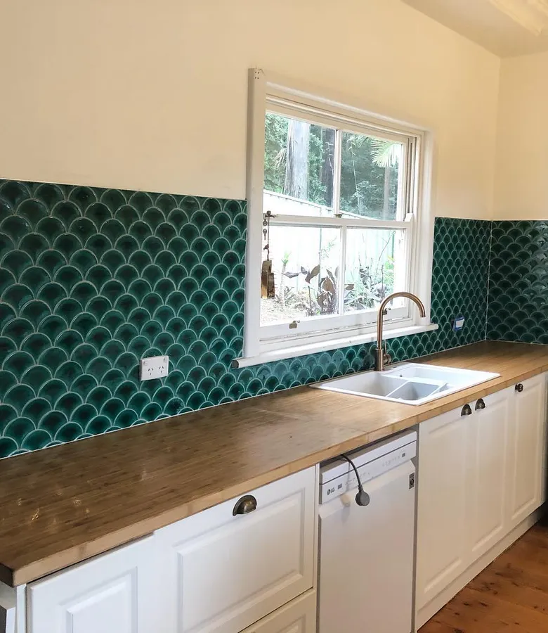 Striking emerald fish-scale kitchen splashback tiles with timber benchtop and white cabinetry