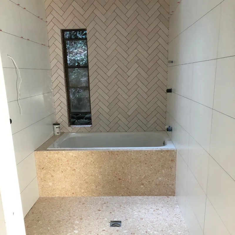 Bathroom feature wall with herringbone tiles and terrazzo bath surround in progress