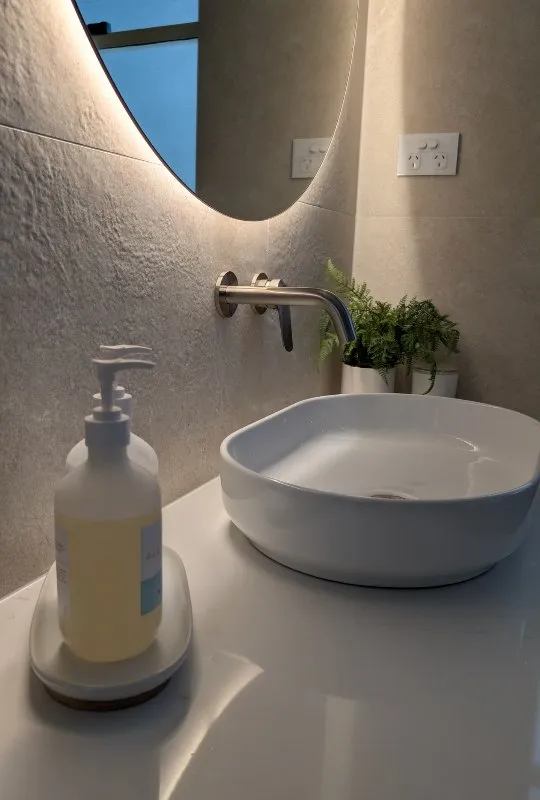 Powder room featuring textured stone wall tiles and elegant backlit round mirror