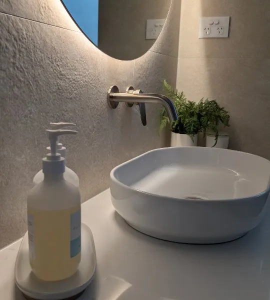 Powder room with textured stone wall tiles and backlit round mirror
