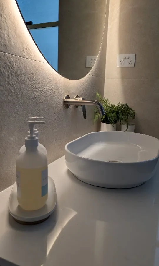 Powder room featuring textured stone wall tiles and elegant backlit round mirror