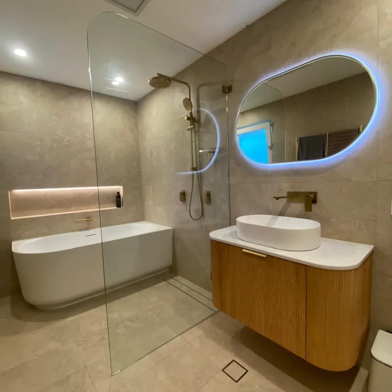 Full bathroom renovation with warm stone tiles, freestanding bath, and gold tapware