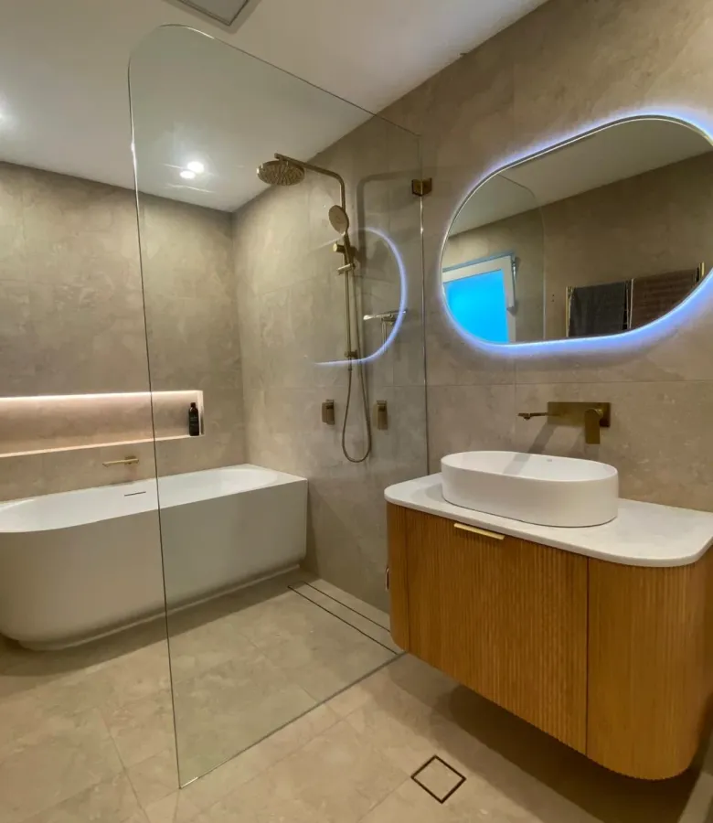Luxury bathroom renovation with large format warm stone tiles, freestanding bath, and gold tapware
