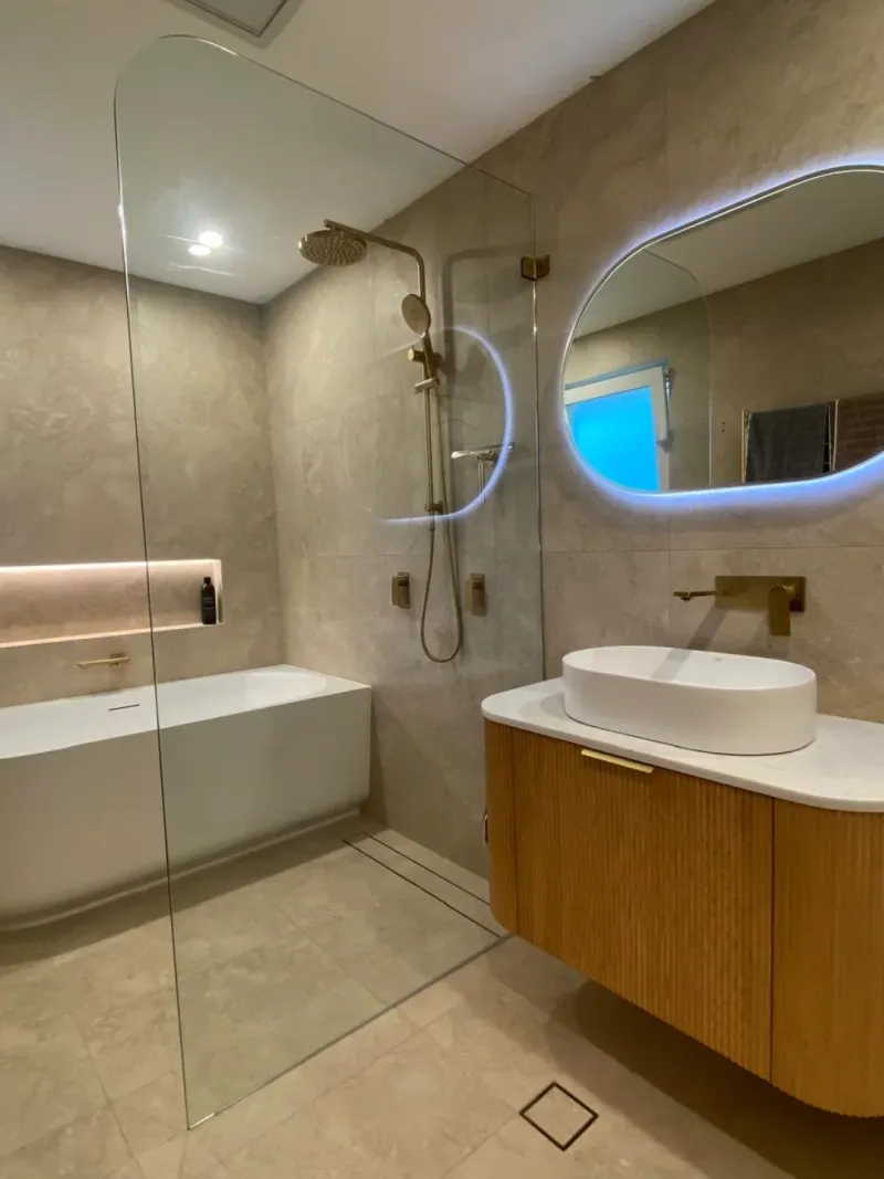 Full bathroom renovation with warm stone tiles, freestanding bath, and gold tapware